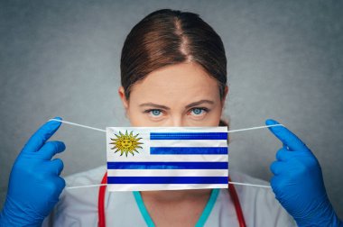 Coronavirus in Uruguay Female Doctor Portrait hold protect Face surgical medical mask with Uruguay National Flag. Illness, Virus Covid-19 in Uruguay, concept photo clipart