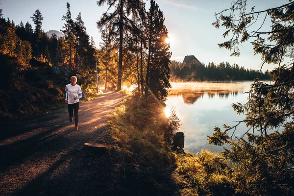 Trail runner in wild nature by lake, gold morning light in background