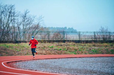 Tıbbi maske takan bir kaçakçı, Avrupa 'da Coronavirus salgını Covid-19. Spor, karantinada aktif yaşam yüz maskesi korumalı cerrahi sterilizasyon. Corona Salgını 'nda atletizm pistinde açık hava koşusu