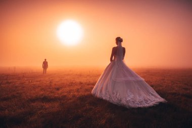 Sonbahar sabahında düğün çifti. Brdie, turuncu sisli gün doğumunda damadı bekliyor. Romantik, evlilik ya da sevgililer günü fotoğrafı. Turuncu düzenleme alanı