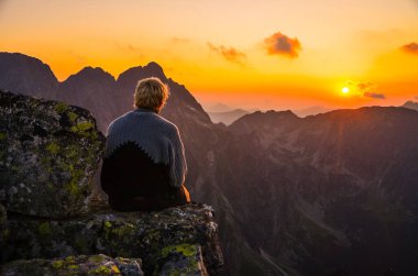 Tepenin tepesinde oturan adam gün batımını seyrediyor. Düşünüyor, sakin, dinlenme konsepti fotoğrafı doğadan.