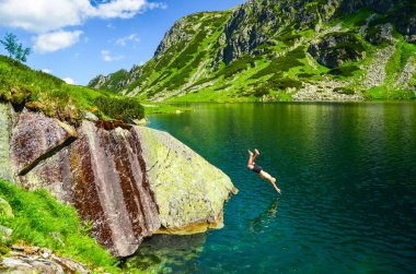 Dağlardaki güzel mavi göle atlayan iki genç adam. Güzel manzarada özgürlükle dolu yaz manzarası