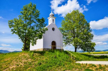 Güneşli bahar günündeki şapel - yeşil ağaçlar ve açık mavi gökyüzü