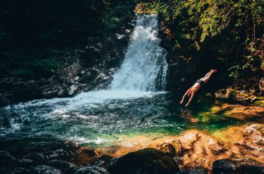 İnsan uçurumdan atlayıp temiz suya atlar vahşi şelalede yeşil yaz doğasında saklanır - cennet manzarası