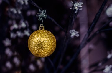 Çiçek ağacında gri, koyu arkaplanı olan altın bir yılbaşı ampulü.