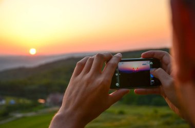 Adam gün batımını cep kamerasıyla çekiyor.