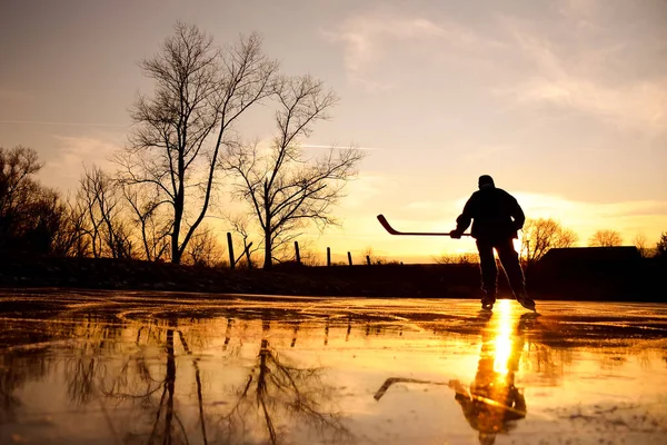 1月の氷結した湖でカラフルな穏やかな冬の日没の間に明るい自然氷の上の若いホッケー選手の反射 — ストック写真