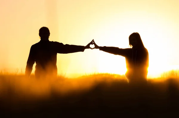 Two young people in love holding hands with shape of heart. Nature scenery, silhouette in rye, wheat field during summer sunrise - valentine or marriage concept photo