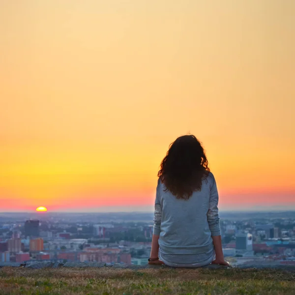 A woman is sitting at ease by the city during sunset moment.