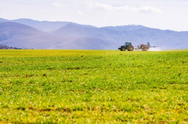 Traktör ilkbahar tarım alanını hazırlıyor ve kirleticiye yardımcı olan böcek ilacı kullanıyor. Bahar tarlasını hazırlıyor ve toprağa yardımcı olan böcek ilacı kullanıyor.