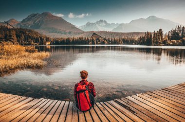 Güzel genç kız, Slovakya 'da, High Tatras' ta, berrak gölün kenarında, harika dağların altında oturuyor. Strbske Pleso Gölü 'nde sabah ışığı. Turistik geziden önce fotoğraf. Özgürlük kavramı