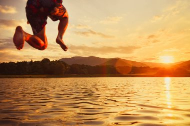 Genç adam sakin yaz günbatımında göle atlıyor..