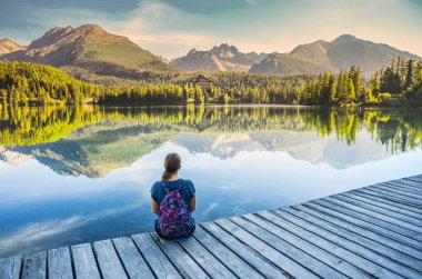 Güzel genç kız, Slovakya 'da, High Tatras' ta, berrak gölün kenarında, harika dağların altında oturuyor. Strbske Pleso Gölü 'nde sabah ışığı. Turistik geziden önce fotoğraf. Özgürlük kavramı