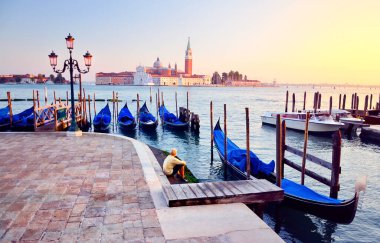 İtalya 'da San Giorgio Maggiore kilisesine karşı Venedik' te Grand Canal 'ın önünde gondolla oturan beyaz elbiseli genç adam. Yaz tatilinden güzel renkli bir sabah ışığı manzarası.