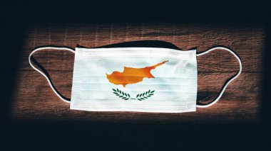 Kıbrıs Ulusal Bayrağı tıbbi, cerrahi, koruma maskesi ve siyah ahşap arka planda. Coronavirus Covid19, enfeksiyonu, hastalığı ya da gribi önleyin. OHAL, tecrit.