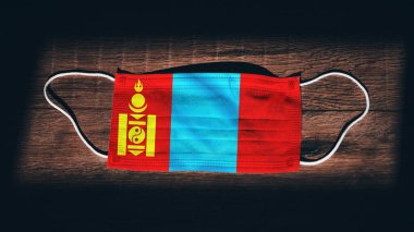 Mongolia National Flag at medical, surgical, protection mask on black wooden background. Coronavirus Covid19, Prevent infection, illness or flu. State of Emergency, Lockdown. clipart