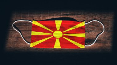 Kuzey Makedonya Ulusal Bayrağı siyah ahşap arka planda tıbbi, cerrahi ve koruma maskesi taşıyor. Coronavirus Covid19, enfeksiyonu, hastalığı ya da gribi önleyin. OHAL, tecrit.