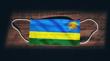 Ruanda Ulusal Bayrağı tıbbi, cerrahi, siyah ahşap arka planda koruma maskesi. Coronavirus Covid19, enfeksiyonu, hastalığı ya da gribi önleyin. OHAL, tecrit.