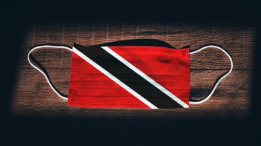Trinidad ve Tobago Ulusal Bayrağı tıbbi, cerrahi, siyah ahşap arka planda koruma maskesi. Coronavirus Covid19, enfeksiyonu, hastalığı ya da gribi önleyin. OHAL, tecrit