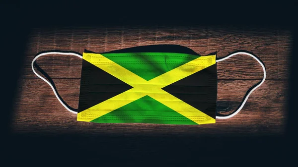 黒い木の背景に保護マスクでジャマイカ国旗 コロナウイルスCovid19 感染を防ぐ 病気やインフルエンザ 非常事態ロックダウン — ストック写真