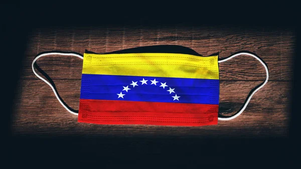 Venezuela National Flag at medical, surgical, protection mask on black wooden background. Coronavirus Covid19, Prevent infection, illness or flu. State of Emergency, Lockdown