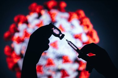 Coronavirus Covid-19 Koruma ve Aşı. Elinde aşı için cam şişeyle Coronavirus arka planında tıbbi eldiven silueti olan bir şırınga, koyu renkli tıbbi tema.
