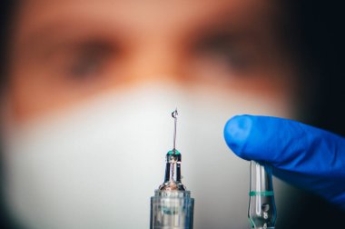 Coronavirus Covid-19 Koruma ve Aşı. Koruyucu kıyafetli ve maskeli bir kadın doktor şırınga ve aşı taşıyor..