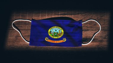 Idaho bayrağı. Coronavirus Covid 19, ABD 'de. Tıbbi maske siyah arka planda izole edildi. Amerika 'da hava enfeksiyonlarına karşı korunmak için yüz ve ağız maskeleri.