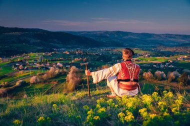Geleneksel Slovak halk kıyafeti giymiş bir adam bahar doğasında oturuyor. Hrinova Slovakya