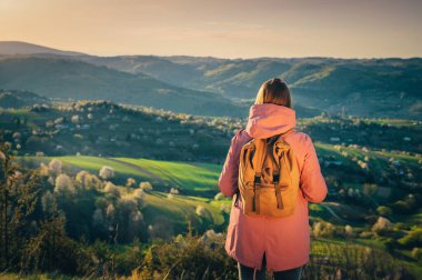 Macera fotoğrafı, yolculuk hipster gezgini. Dişi turist ya da yürüyüşçü arka planda güzel bir bahar manzarasına bakıyor. Seyahat fotoğrafı, antika sırt çantası, sırt çantası. Alıntı veya montajınız için boşluk düzenleyin
