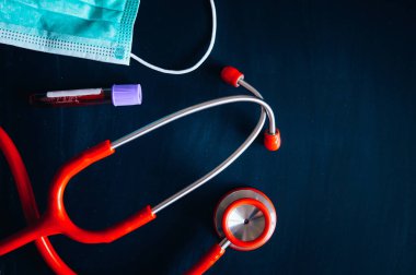 Coronavirus koruma konsepti fotoğrafı. Siyah tahtada kırmızı stetoskop ve beyaz cerrahi maske, metin için siyah düzenleme alanı.