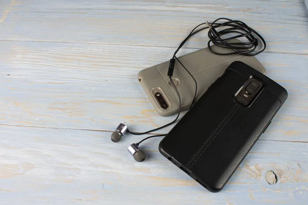 Eski ahşap bir arka planda duran kulaklıklı iki akıllı telefon.