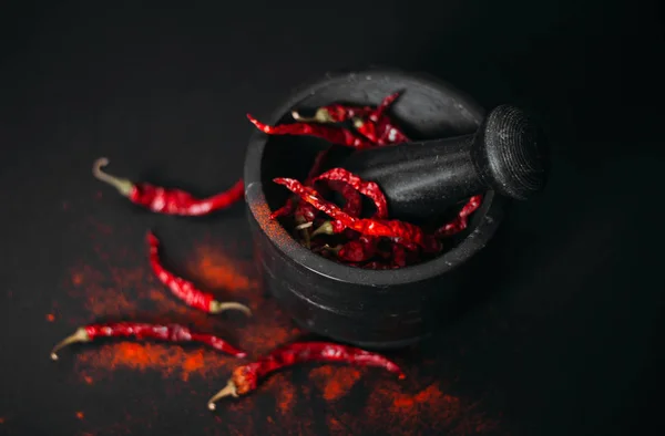 Dry red spicy peppers and powder in stone mortar