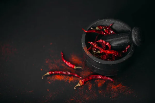 Dry red spicy peppers and powder on black.