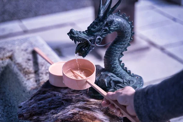 A visitor of a Shinto Shrine is holding water ladle about to purify their hands with water from Chozuya. Dragon sculpture dripping water fountain.