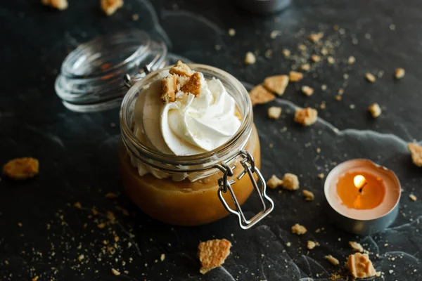 Delicious dessert in a jar. Banana dessert with caramel and whipped cream, garnished with cookies and nuts. Romantic composition with candles
