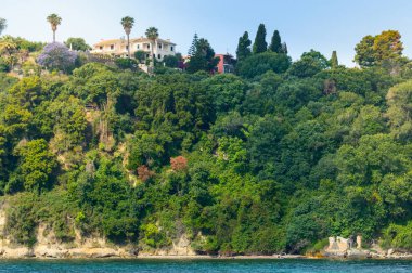 Ev bir dağın tepesine inşa edilmiş, yamaçta ağaçlar var..