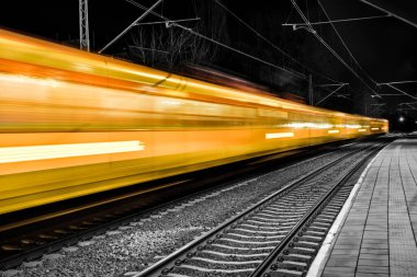 Tren istasyonundan geçen sarı bir ekspres tren daha küçük duraklarda durmaz. Platform boyunca uzun demiryolu rayları.