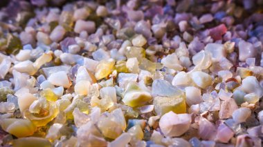 Jeolojik örnekler masanın üzerindeki bir kaba saçılmış, küçük renkli çakıl taşları ışıkta renk değiştiriyor..