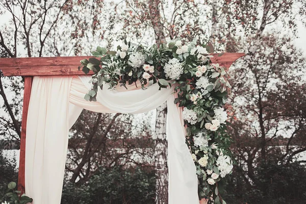 Floral arch with cloth and wooden elements at a rustic wedding ceremony