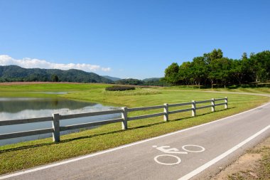 Göl parkındaki bisiklet yolu mavi gökyüzü ve dağ ormanı arka planıyla.
