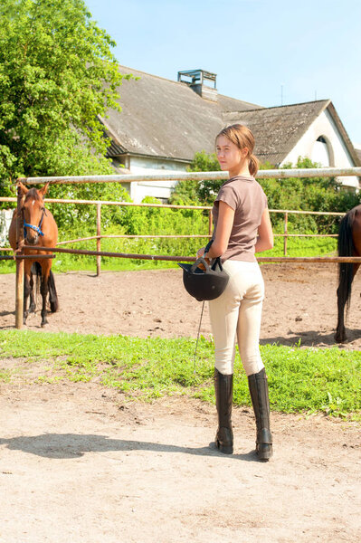 Young teenage girl equestrian standing outdoors. Multicolored su