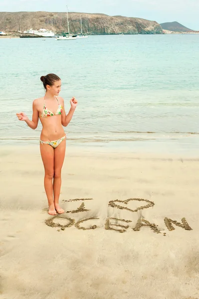 Молодая девушка-подросток с я люблю океан сообщение на песке — стоковое фото