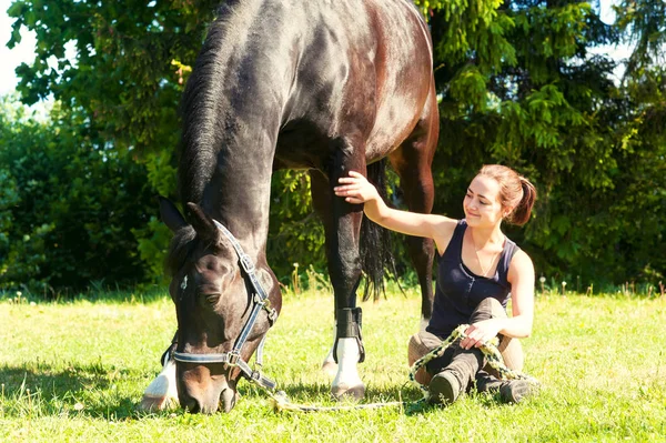 Mladá žena jezdecké sedí blízko svého koně na trávě — Stock fotografie