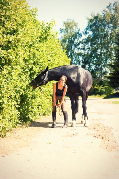 Černý koně jíst bush opustí blízko mladá dáma jezdecké — Stock fotografie