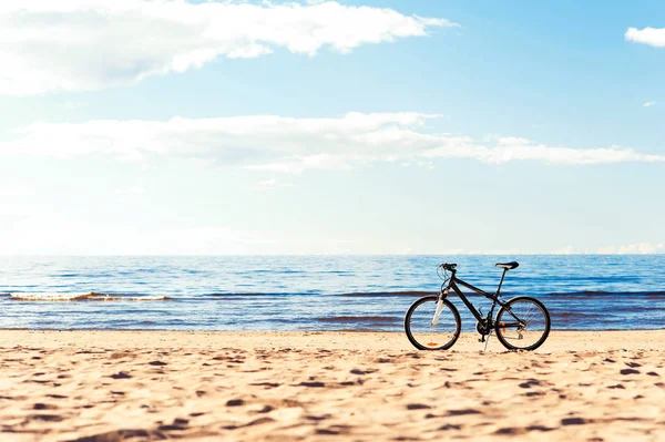 Una bicicleta de pie en la arena de la playa en el fondo azul del paisaje marino —  Fotos de Stock
