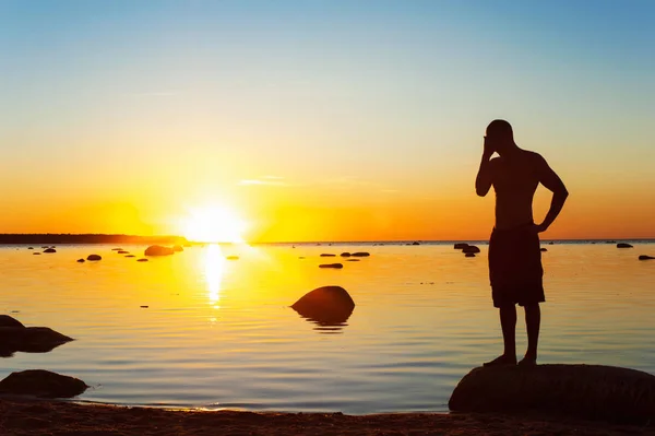 Junge sportliche Männersilhouette, die bei Sonnenuntergang am Strand steht — Stockfoto