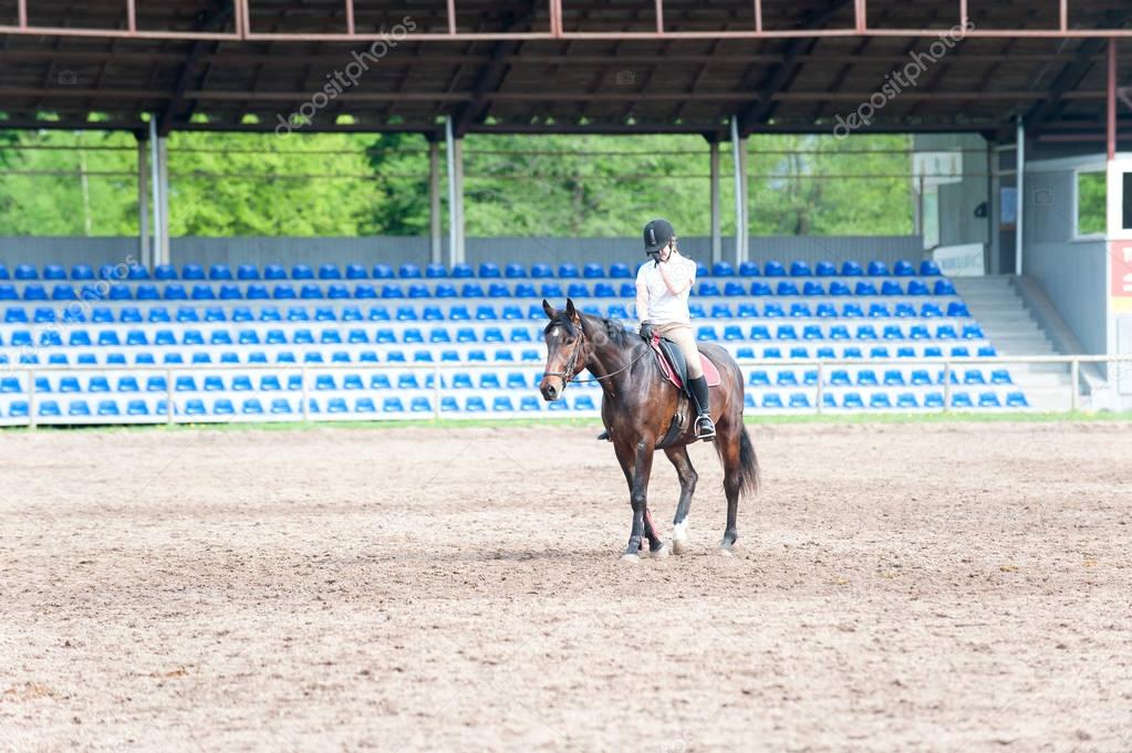 Young teenage girl riding a horse after training on arena
