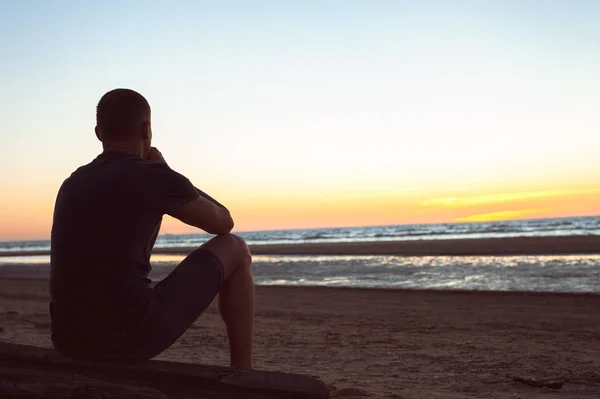 Oppresso da preoccupazioni invisibili. Triste uomo solitario siede sulla spiaggia — Foto Stock