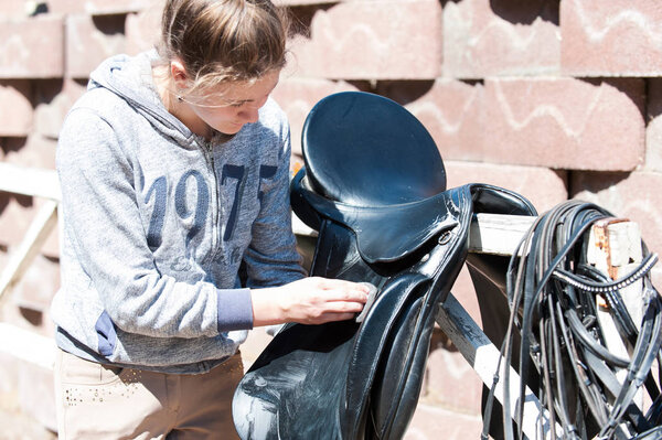 Teenage girl equestrian cleans black Leather Horse Saddle